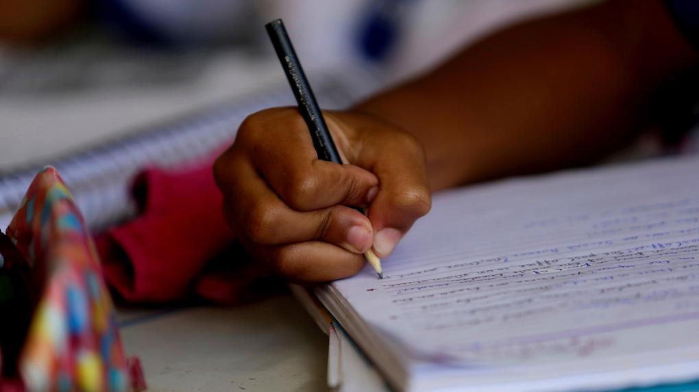 Mão de criança negra escrevendo com lápis em um caderno