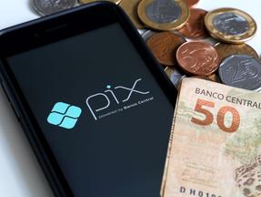 tela de celular indicando o nome pix ao lado de nota de 50 reais e moedas